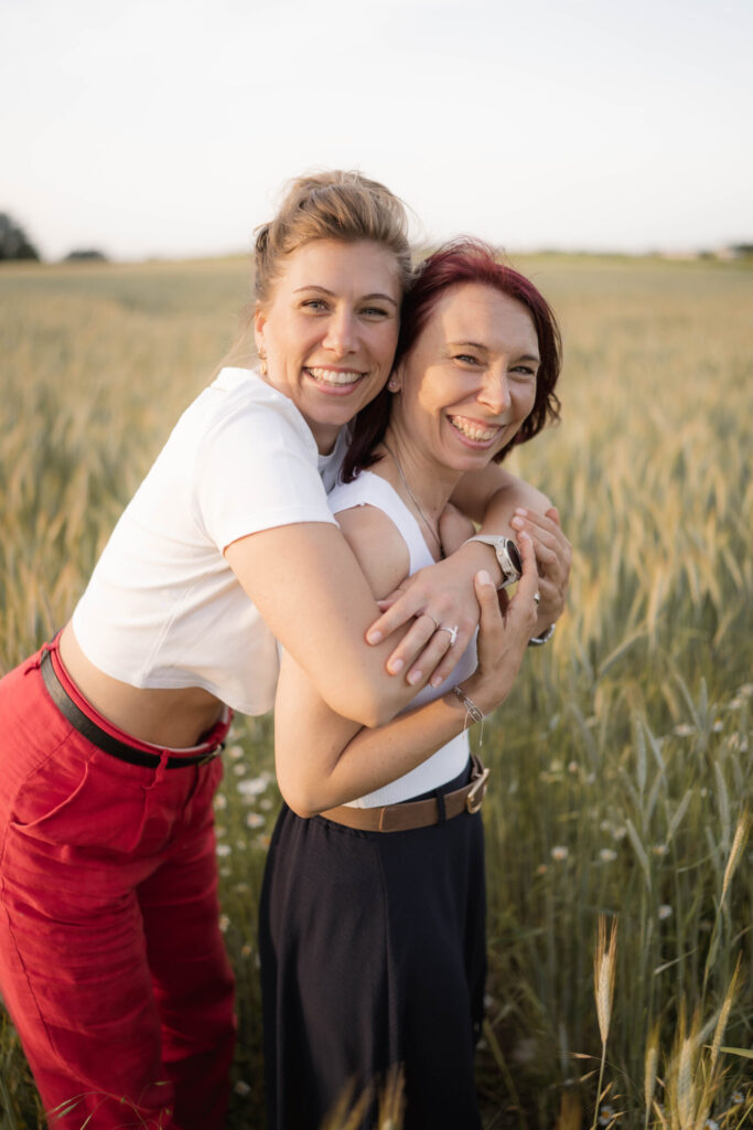 Familienfotografin-Niederoesterreich-groessere-schwester-umarmt-kleinere-in-weizenfeld-von-hinten