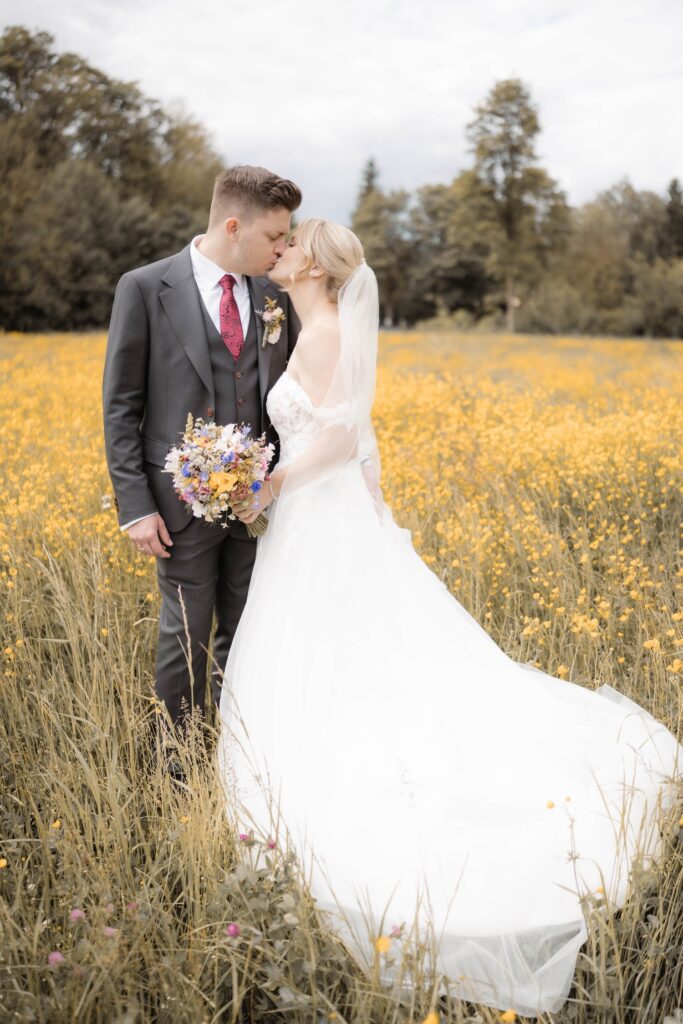 paarshooting-brautpaar-in-gelbem-blumenfeld-kuesst-sich-hochzeitsfotografin-niederoesterreich