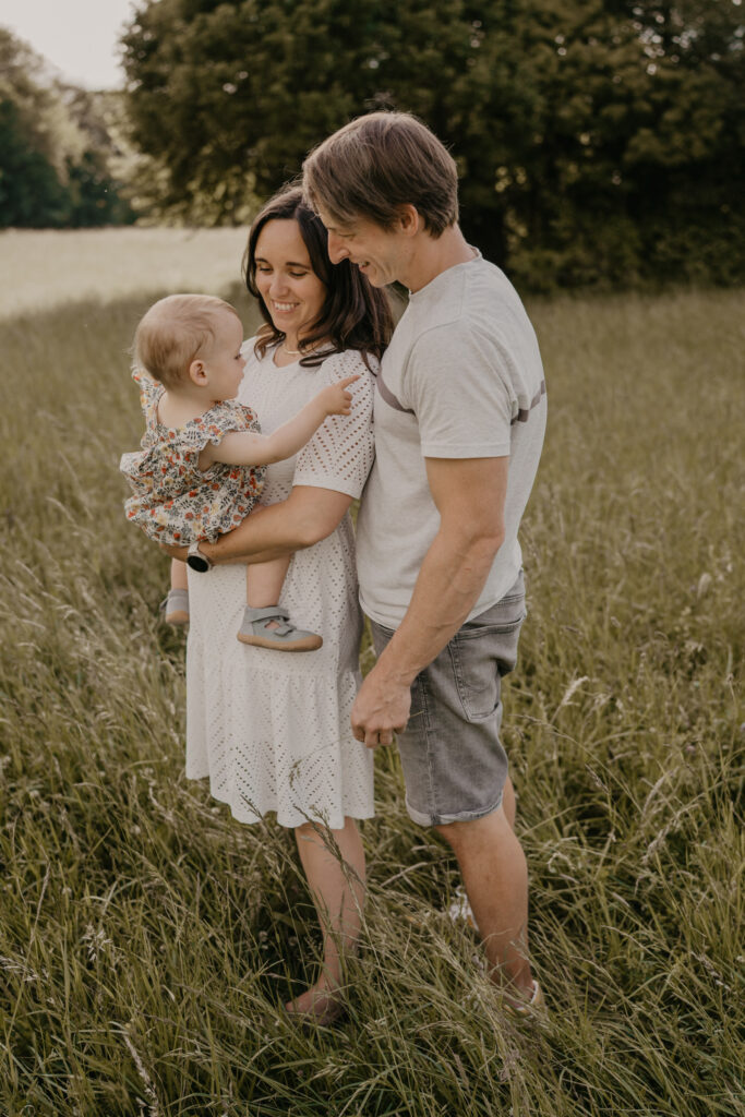 familienshooting-outdoor-mutter-haelt-kind-vater-steht-dahinter
