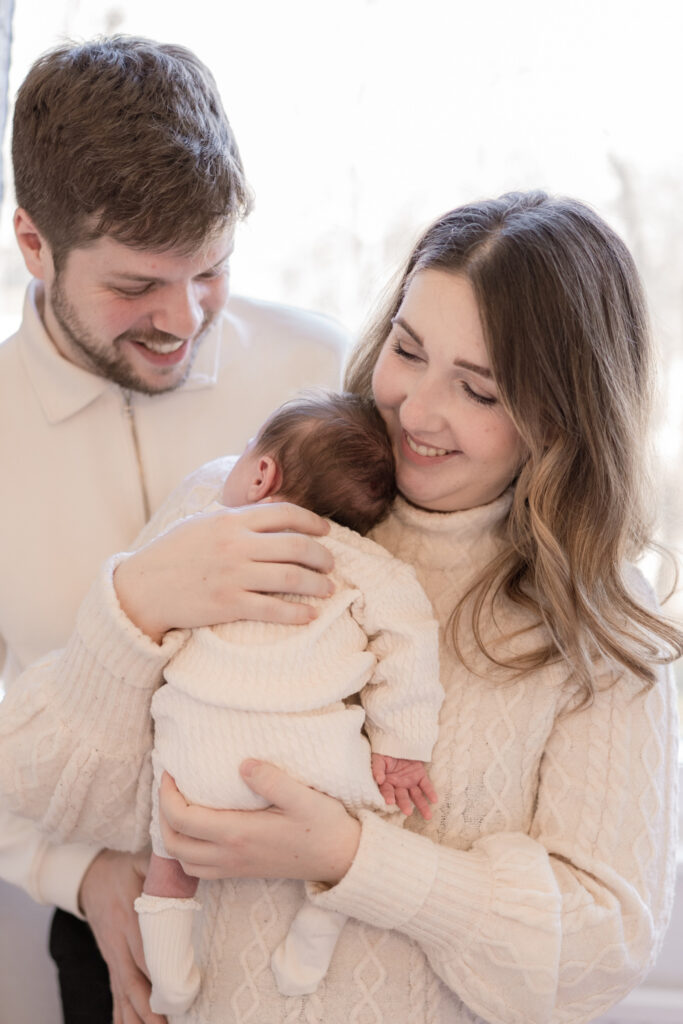 mutter-haelt-baby-mit-kopf-an-schluesselbein-vater-dahinter-nahaufnahme-newborn-shooting